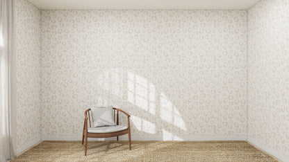 A minimal room with Hallie Leopard Print Wallpaper Repeat Pattern in beige, a brown wooden chair with a gray cushion, woven rug flooring, and sunlight casting window shadows on the wall.