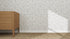 A wooden dresser stands on a woven carpet against a white wall decorated with Hallie Leopard Print Wallpaper Repeat Pattern in light blue. Sunlight casts a triangle-shaped shadow across the playful wallpaper.