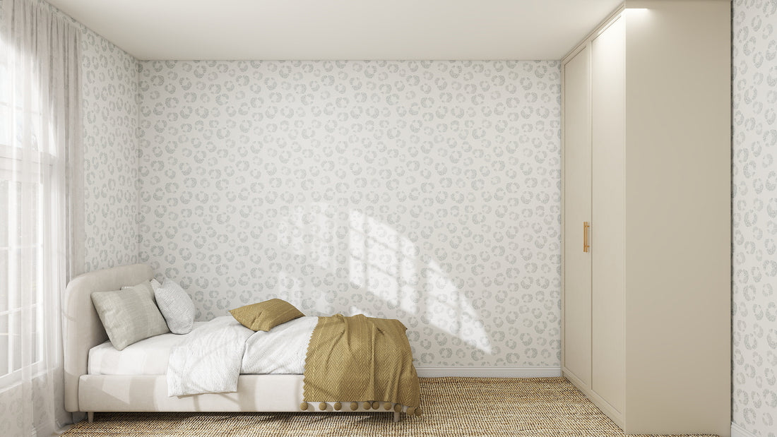 A minimal bedroom features a bed with white and beige bedding, beige pillows, tan throw, woven rug, built-in beige wardrobes, and sunlight streaming through sheer curtains. The Hallie Leopard Print Wallpaper in Light Blue adds playful charm.