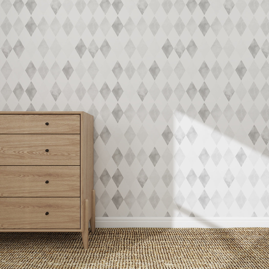 A wooden dresser with five drawers stands on a textured rug beside a wall covered in Harlequin Watercolour Wallpaper Repeat Pattern in grey. Sunlight highlights a patch of the patterned wall.