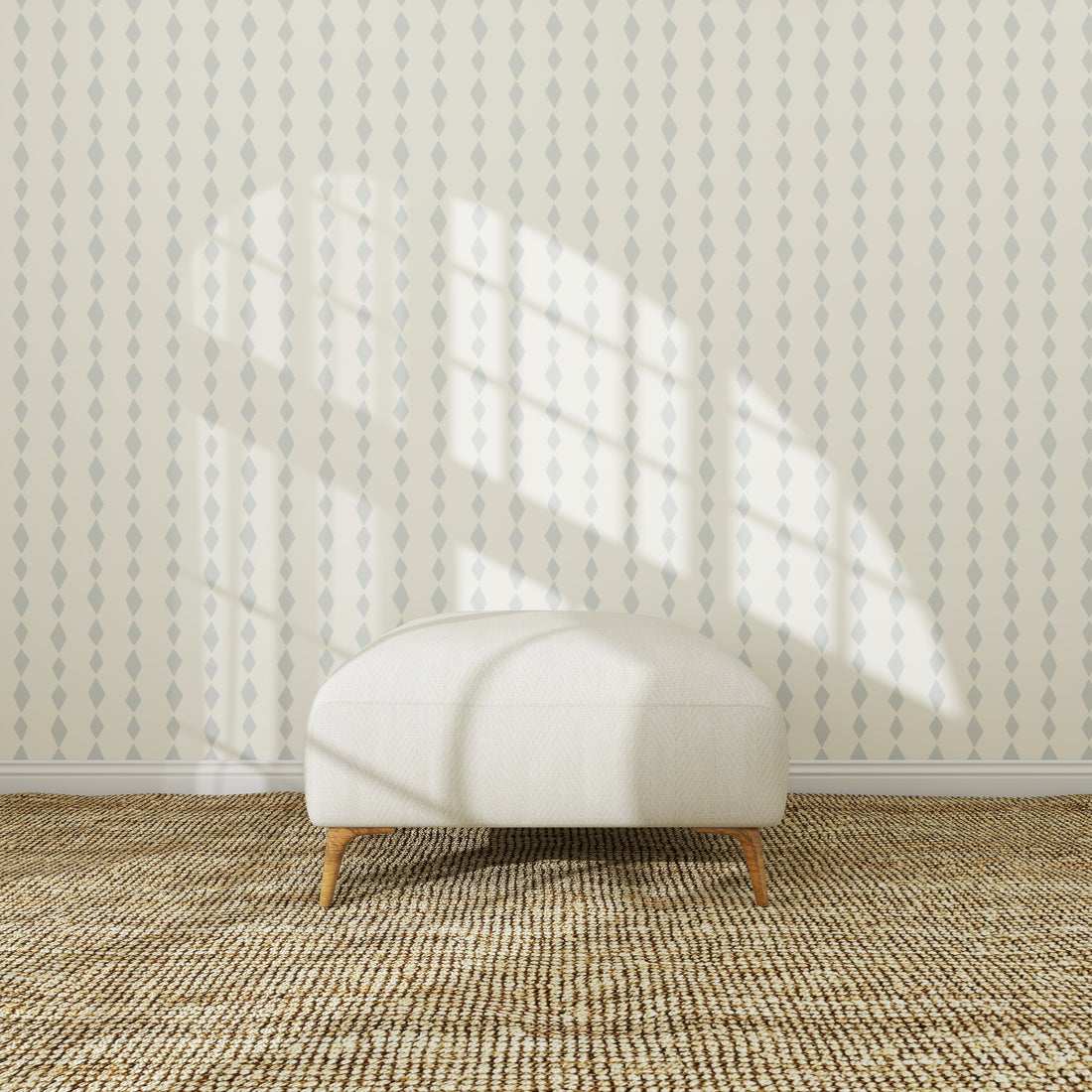 A white oval ottoman with wooden legs sits on a textured carpet in front of Jolly Jester Wallpaper Repeat Blue, as sunlight highlights the wallpaper and casts window shadows, creating a bright and cozy atmosphere.