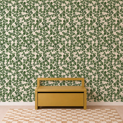 A yellow bench sits against a wall adorned with the “How Lucky We Are Clovers Wallpaper,” featuring lush green leaves. The floor showcases a beige and white checkerboard rug, enhancing the simple and well-lit setting. With its minimalist, modern style, this space could easily serve as inviting nursery wallpaper inspiration.