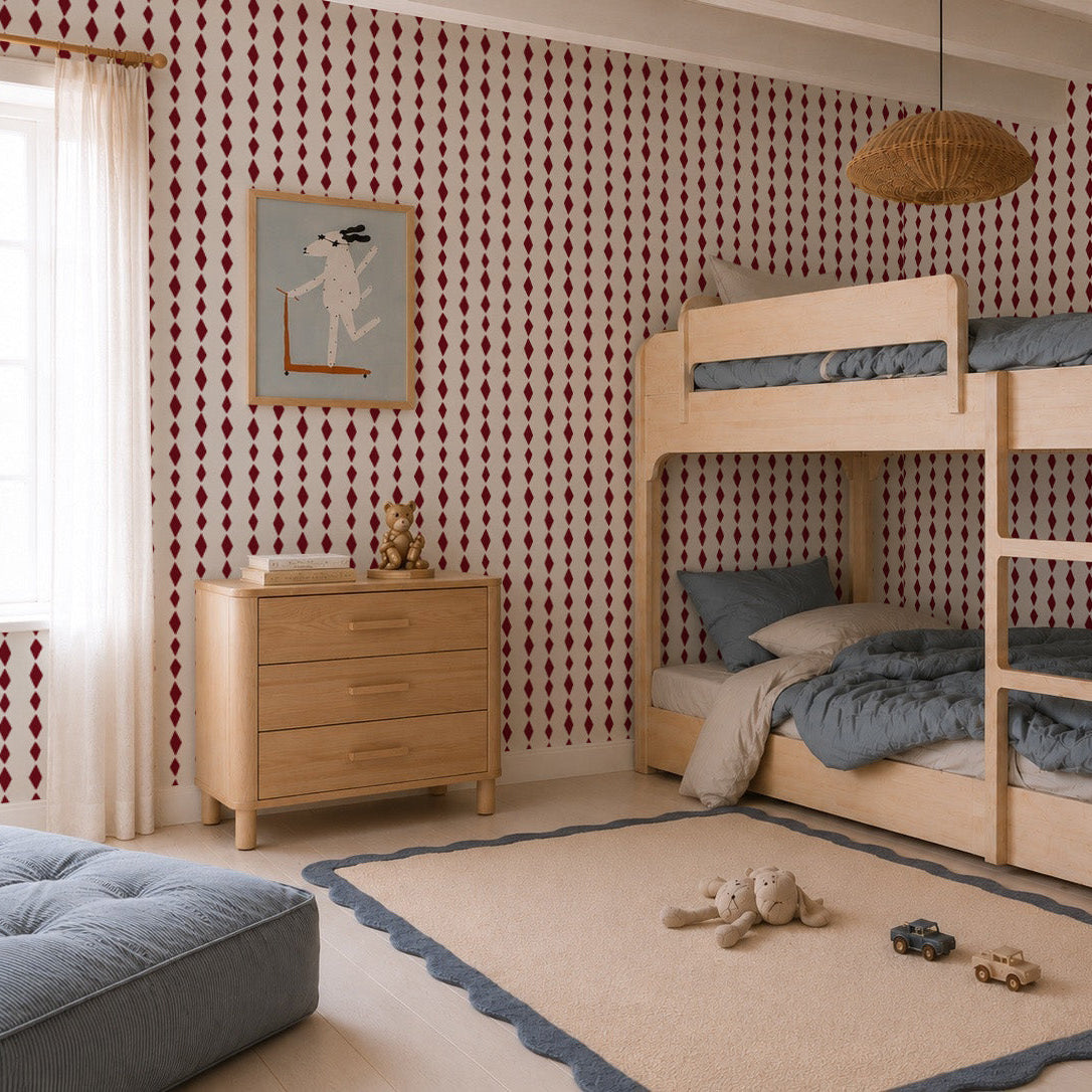 Children’s bedroom featuring a wooden bunk bed, gray bedding, dresser, soft rug, plush toys, and the Jolly Jester Wallpaper Sample in Cherry—its vibrant red and white pattern highlighting the wallpaper&