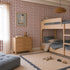 Children’s bedroom featuring a wooden bunk bed, gray bedding, dresser, soft rug, plush toys, and the Jolly Jester Wallpaper Sample in Cherry—its vibrant red and white pattern highlighting the wallpaper&