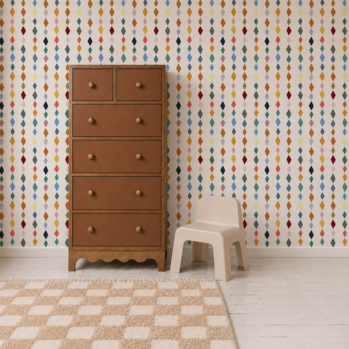 A wooden dresser and small plastic chair set against a wall featuring Jolly Jester Wallpaper, Multi, which displays a pattern of small, colorful vertical diamonds on a light background.