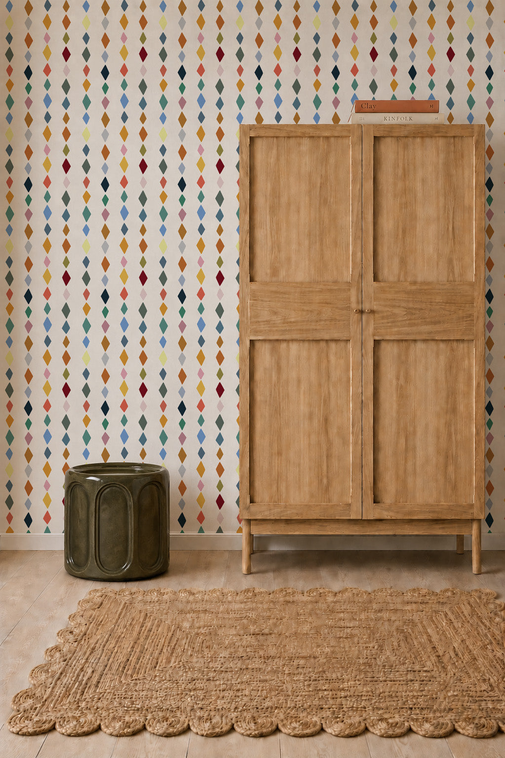 Jolly Jester Wallpaper, Multi featuring a repeating pattern of small, multicolored diamonds on a white background, next to a tall wooden cabinet and a dark green cylindrical stool.