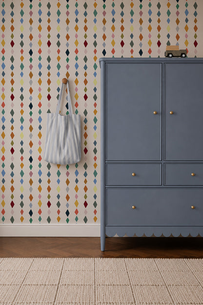 Jolly Jester Wallpaper, Multi, featuring a vertical pattern of small, colorful blue, red, yellow, and green diamonds, with a blue wardrobe and a striped tote bag hanging on the wall.