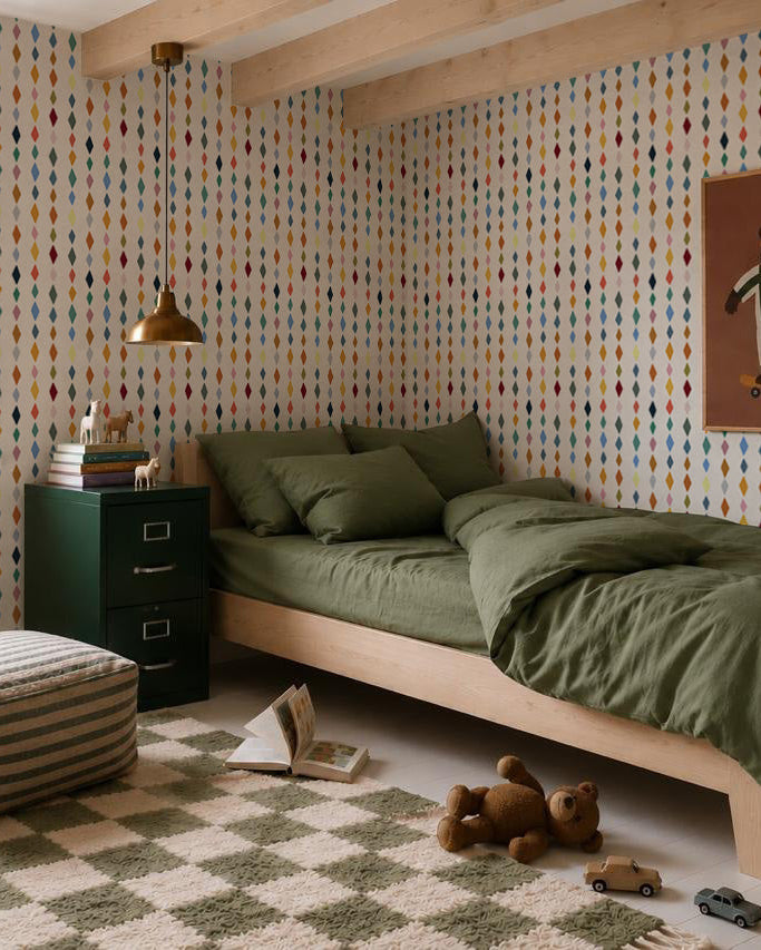 A cozy bedroom with a wooden bed and olive green bedding, a green cabinet, checkered rug, soft toys, and playful Jolly Jester Wallpaper, Multi. A gold lamp hangs above the bed.