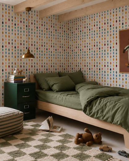 A cozy bedroom with a wooden bed and olive green bedding, a green cabinet, checkered rug, soft toys, and playful Jolly Jester Wallpaper, Multi. A gold lamp hangs above the bed.