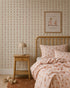 Cozy bedroom with a wooden bed, polka dot bedding, matching rug, small wooden nightstand with a beige lamp, and a framed cute animal print on charming Jolly Jester Wallpaper in pink.