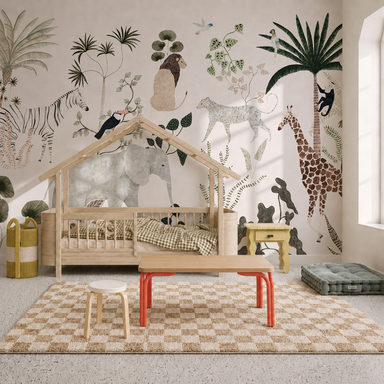 Children’s room with a house-shaped bed, checkered rug, small tables, and a wall mural featuring illustrated jungle animals like giraffes, elephants, and zebras. Light streams in through a large window, highlighting the playful Jungle Dreams Mural that brings the nursery to life.