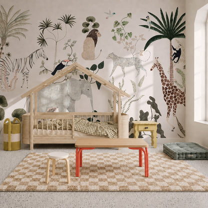 Children’s room with a house-shaped bed, checkered rug, small tables, and a wall mural featuring illustrated jungle animals like giraffes, elephants, and zebras. Light streams in through a large window, highlighting the playful Jungle Dreams Mural that brings the nursery to life.