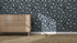 A wooden dresser sits on a woven rug next to a wall covered in Blue Leopard Print Wallpaper | Sample, with sunlight casting shadows that highlight the bold, stylish look of the room.