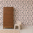 A brown dresser stands on a light rug next to a small beige chair and stool, set against a pink wall adorned with the Leopard Print Wallpaper, featuring a quirky black and white irregular dot pattern reminiscent of leopard spots.