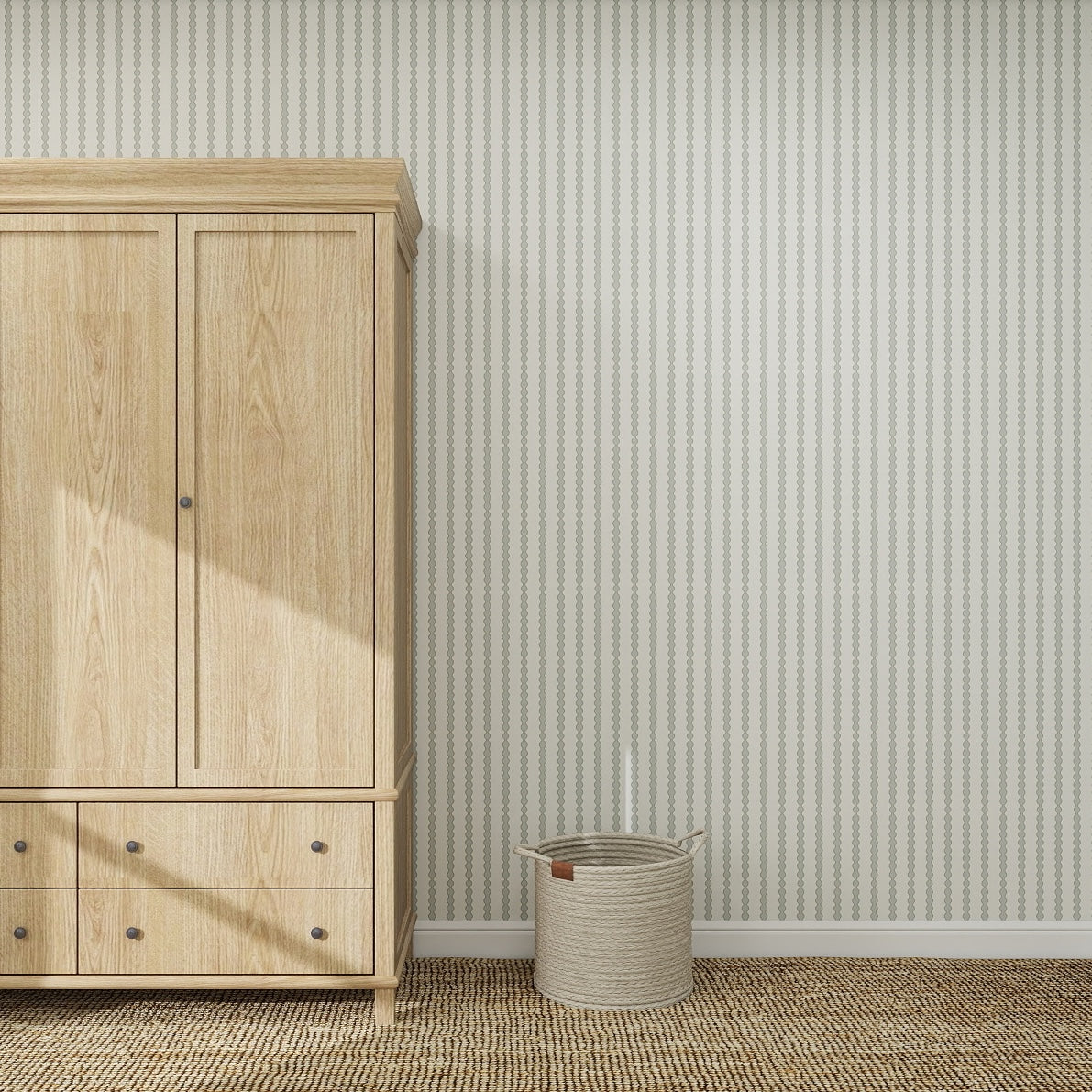 A light wood wardrobe stands on a woven rug next to a beige basket with a leather handle, against a wall adorned with Little Abacus Stripe Blue and Green nursery wallpaper for a charming touch.