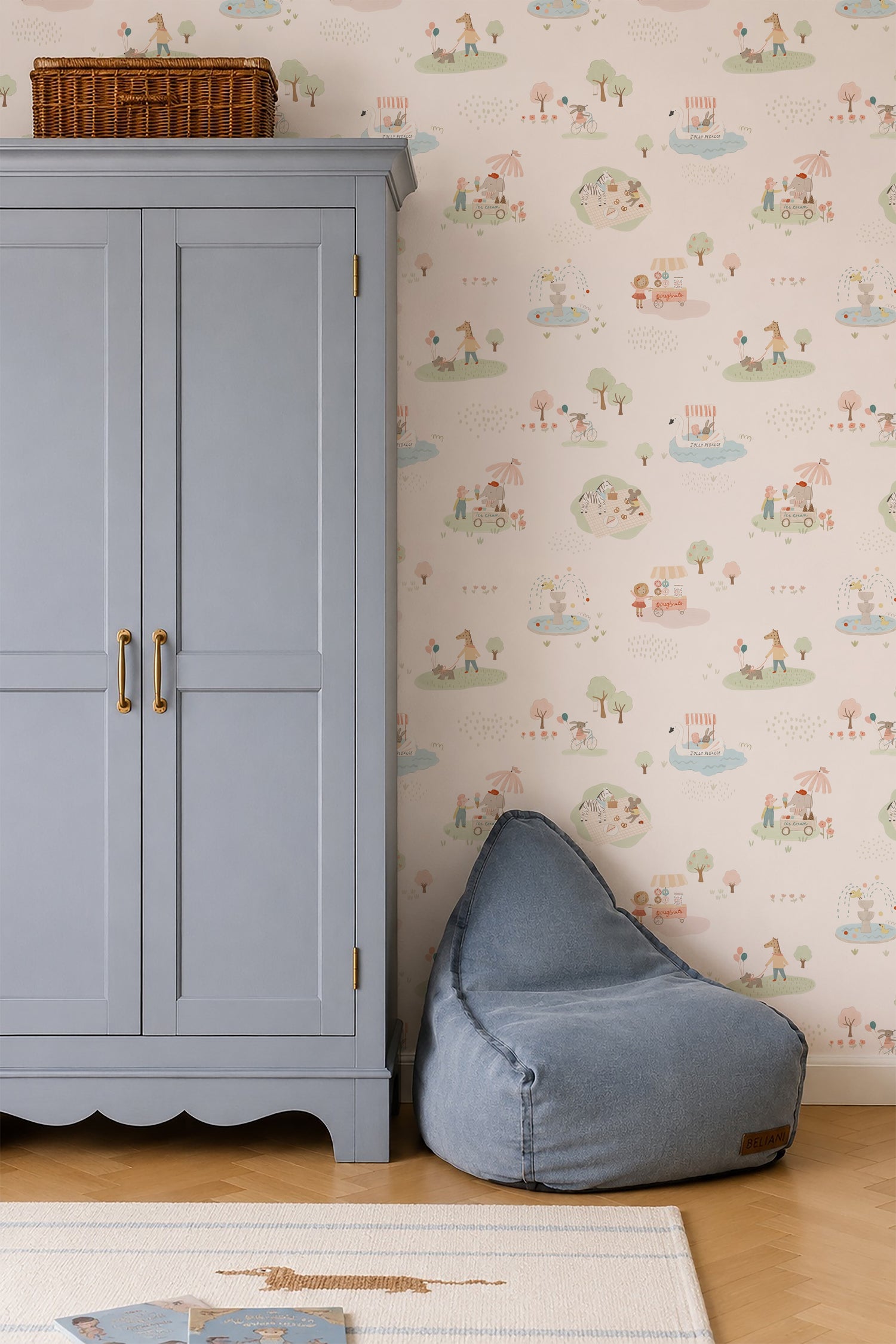 A light blue wardrobe with gold handles stands beside a blue bean bag chair on a wood floor, against a wall decorated with Little Friends Day Out Wallpaper. A wicker basket sits atop the wardrobe.