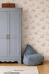 A light blue wardrobe with gold handles stands beside a blue bean bag chair on a wood floor, against a wall decorated with Little Friends Day Out Wallpaper. A wicker basket sits atop the wardrobe.