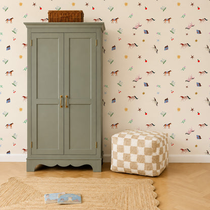 A sage green armoire stands against Little Paddock Wallpaper featuring horses, houses, stars, and flowers, with a checkered pouf and a woven rug on the floor.