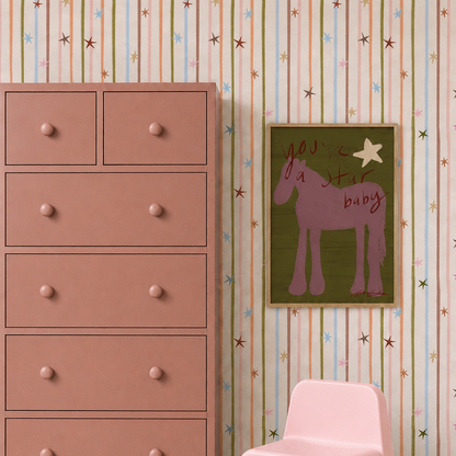 A dusty pink dresser stands against Starlight Stripe Wallpaper, featuring vertical multicolored stripes and small stars, with a framed horse illustration hung on the wall.
