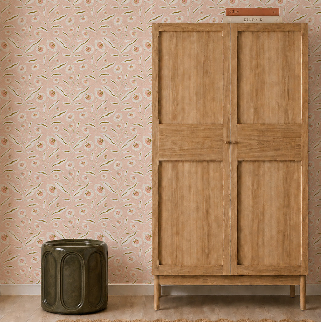 A wooden wardrobe stands next to a green ceramic stool against whimsical wall decor featuring Matildas Sunflower Wallpaper, Pink, in a minimalist room with a light wood floor.