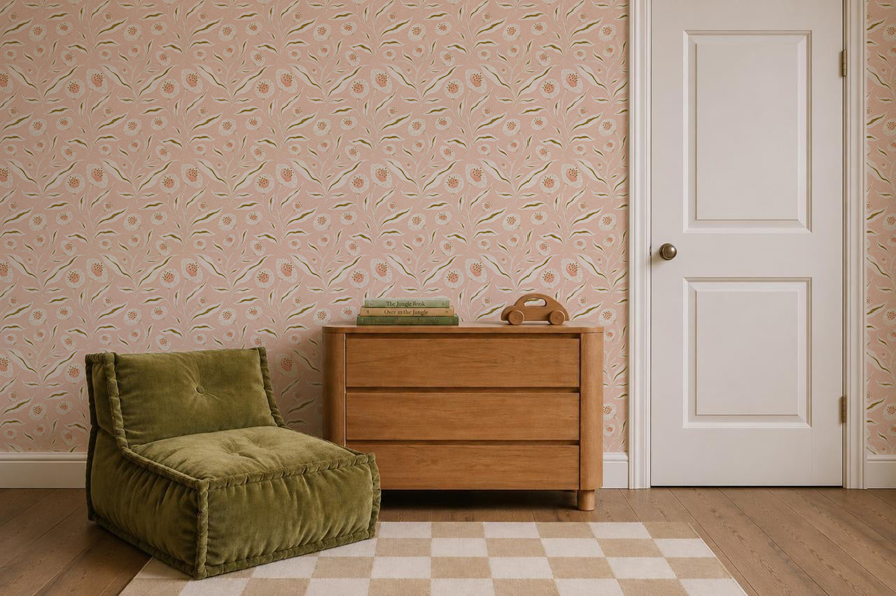 A cozy room with a green cushioned chair, wooden dresser with books on top, a white door, Matildas Sunflower Wallpaper in pink featuring delicate floral patterns on the walls, and a beige checkered rug on a wooden floor.
