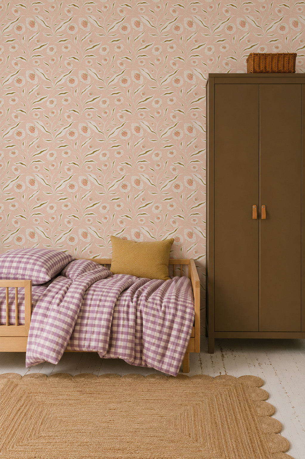A cozy bedroom with a wooden toddler bed, purple checkered bedding, a yellow pillow, brown wardrobe, Matildas Sunflower Wallpaper in pink adding whimsical wall decor, and a woven rug on a white wooden floor.