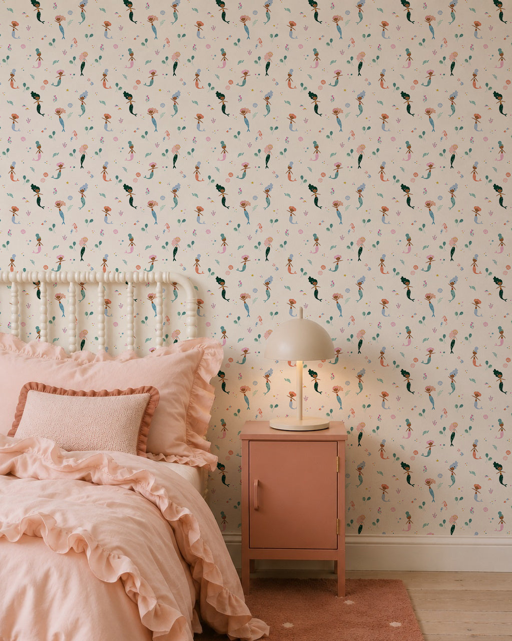 A cozy bedroom featuring Mermaid Friends Wallpaper, a ruffled pink bedspread with matching pillows, and a pink nightstand topped with a round lamp for a charming, playful look.