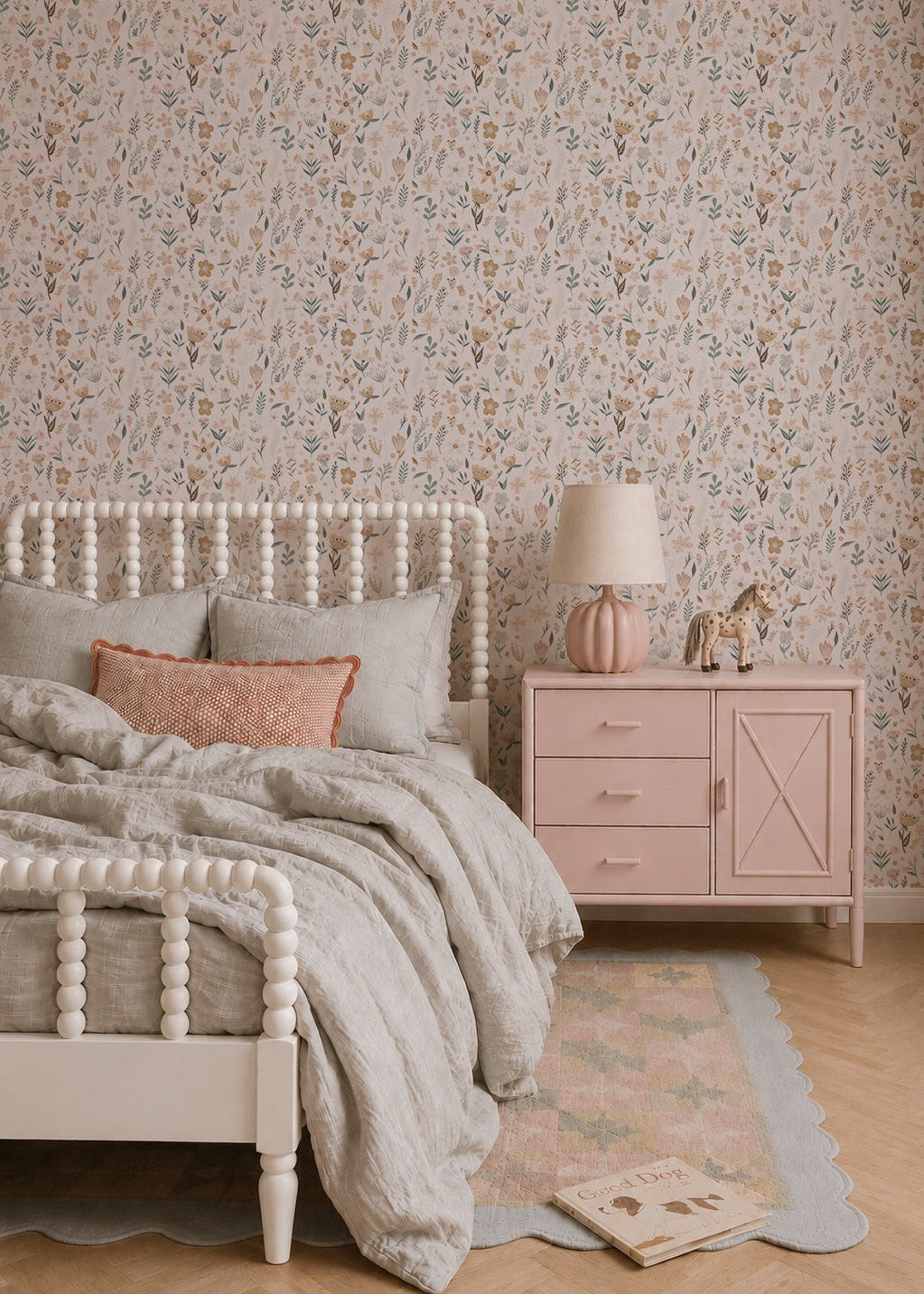 A cozy bedroom features a light wood bed, soft gray bedding, and pastel decor. Millie Floral Wallpaper and a pink nightstand add gentle charm, while a toy giraffe rests beneath the warm glow of a pink lamp.