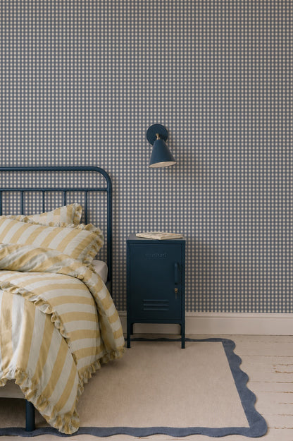 A dark blue metal locker-style bedside table sits next to a bed with yellow striped bedding against Mini Check Wallpaper, Deep Blue.