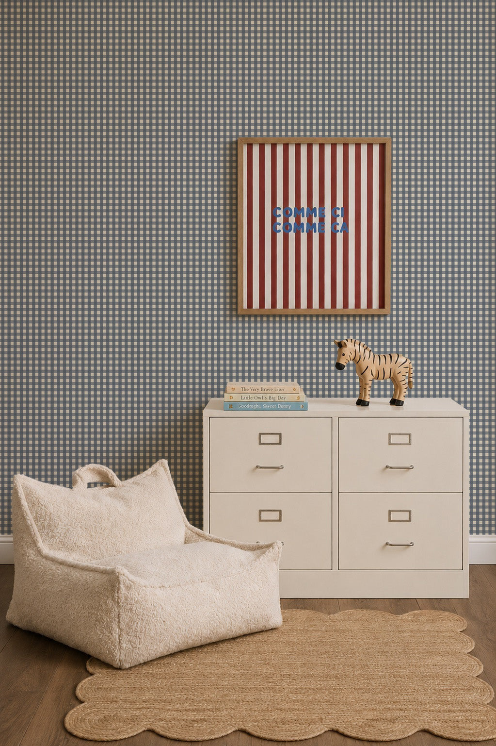 A cozy corner featuring a cream-colored lounge chair, a small metal filing cabinet with a wooden zebra figurine and books on top, and a framed red and white striped print hanging on Mini Check Wallpaper, Deep Blue.