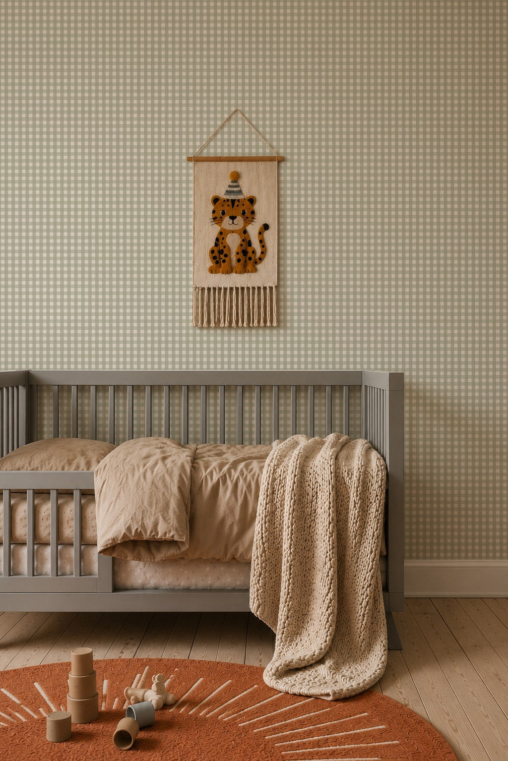 A grey crib with beige bedding and a knitted throw blanket sits against Mini Check Wallpaper, Green, featuring a felt leopard wall hanging above it and a round rug on the floor.