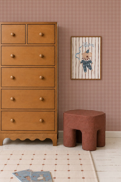 A wooden dresser sits next to a small, chunky stool and a framed illustration of a circus mouse against Mini Check Wallpaper, Red.
