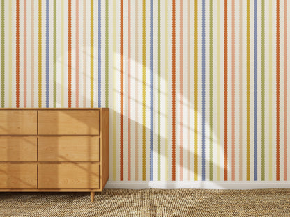 A wooden dresser stands on a beige carpet beside a wall decorated with the Mini Scallop Stripe Wallpaper Repeat Pattern | Multi. Sunlight casts window shadows across the wall and part of the dresser.