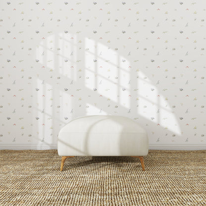 A simple white ottoman sits on a woven rug in front of a white wall adorned with Mollys Flower Garden Wallpaper Repeat | Sample. Sunlight streams in, casting a window-shaped shadow above the ottoman.