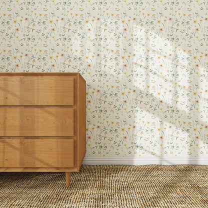 A wooden dresser stands on a woven rug against a wall decorated with Morning Meadow Wallpaper. Sunlight pours in through the window, casting gentle shadows on the hand-painted wallpaper and the floor below.