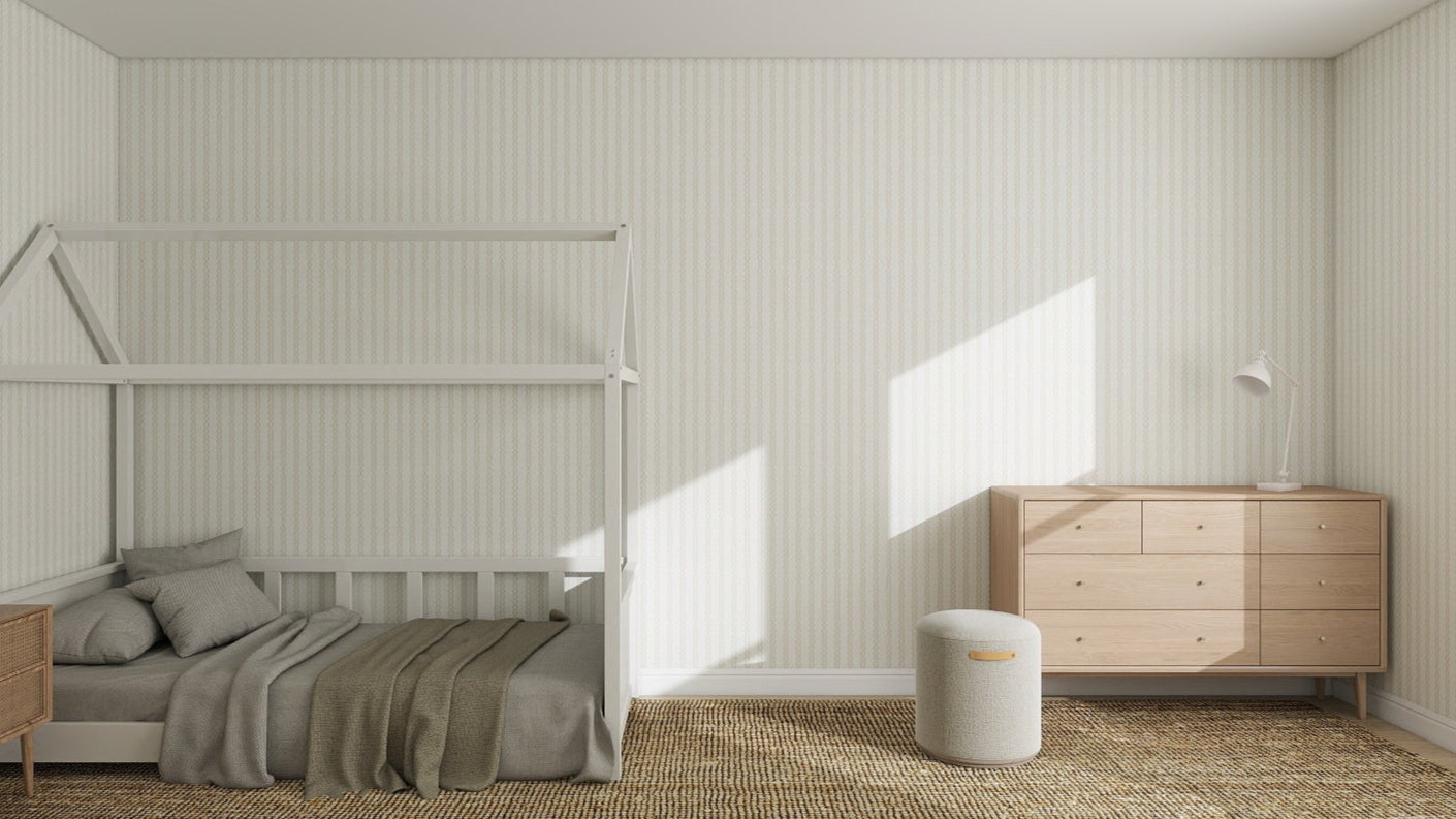 A minimalist bedroom features a house-shaped bed frame, neutral bedding, wooden dresser, nightstand, and walls adorned with Little Abacus Stripe Off White and Taupe Wallpaper, all enhanced by soft-toned rugs and abundant natural light.