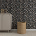 A beige cabinet with a toy fox and books stands against the Millie Floral Wallpaper Repeat Pattern in Charcoal, with a woven basket nearby on a light textured rug, creating a charming update.