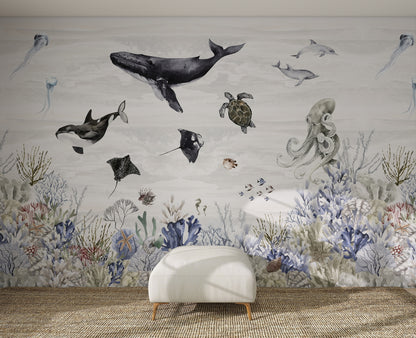 A white ottoman sits on a woven rug in front of the Ocean Magic Mural, Watercolour, featuring illustrated ocean animals like a whale, orca, turtle, rays, octopus, and fish swimming above vibrant coral and sea plants.