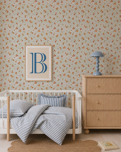 A cozy children’s bedroom with a small white bed, blue-striped bedding, round rug, wooden dresser with a blue lamp, and Ollies Oranges Wallpaper in Blue. A framed print featuring a large blue letter “B” hangs on the wall.