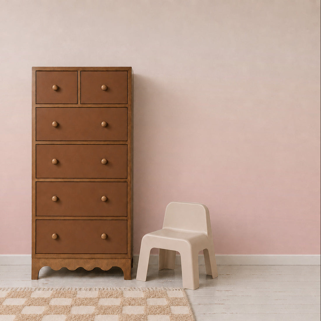 A tall wooden dresser with six drawers and round knobs stands next to a small beige plastic chair on a light wood floor with a patterned rug, set against the Ombre Mural Sample in Pink, which beautifully showcases the subtle colour and quality of the wallpaper.