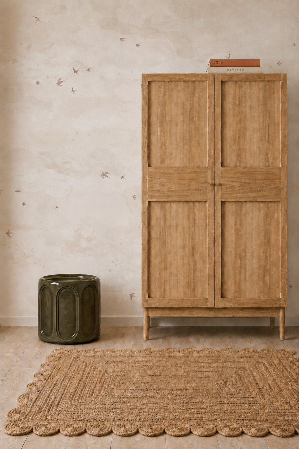A wooden armoire, a green cylindrical stool, and a woven rug set against Opals Sky Birds Mural, Sand wallpaper.