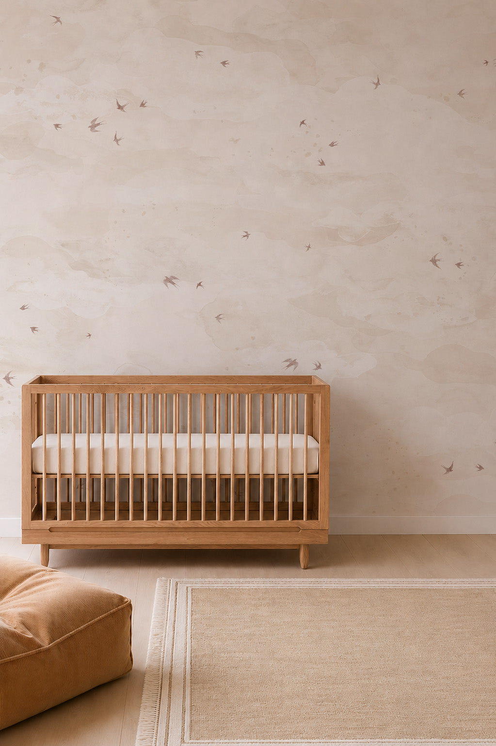 Wooden crib against a wall with Opals Sky Birds Mural, Sand, featuring a soft, cloudy pattern and scattered birds in flight.