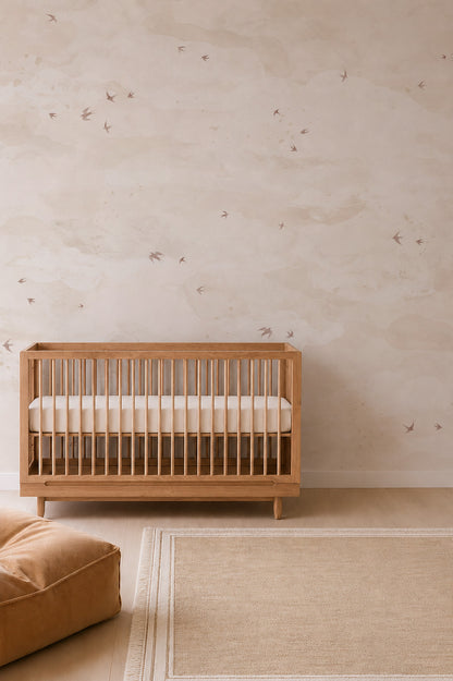 Wooden crib against a wall with Opals Sky Birds Mural, Sand, featuring a soft, cloudy pattern and scattered birds in flight.