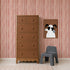 A brown dresser stands beside a small gray chair and a framed cartoon dog art on a wall adorned with Painted Stripe Wallpaper, Red, complemented by a beige carpet on the floor.