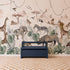 A children’s room featuring the Paradise Jungle Mural, an illustrated wallpaper showcasing jungle animals like giraffes, elephants, lions, zebras, and birds surrounded by lush leaves, paired with a blue bench and a checkered rug on the floor.