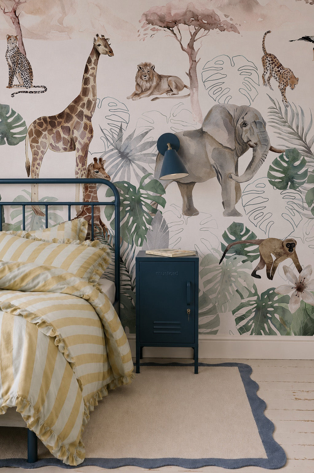 A children’s bedroom with a yellow and white striped bed, blue nightstand, and vibrant Paradise Jungle Mural featuring playful giraffes, elephants, lions, cheetahs, monkeys, and lush tropical leaves.
