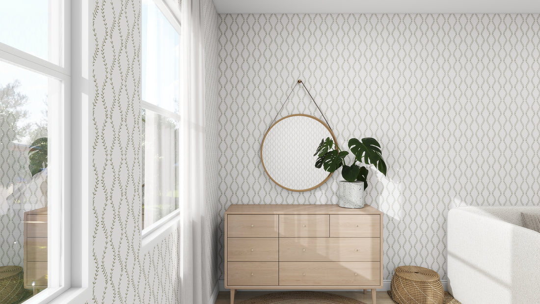 A minimalist room showcases a wooden dresser with a round mirror above and a potted plant nearby. The Vintage Vines Wallpaper Repeat Pattern by munks and me brings subtle charm as natural light pours in from the window on the left, while an elegant woven basket rests on the floor.