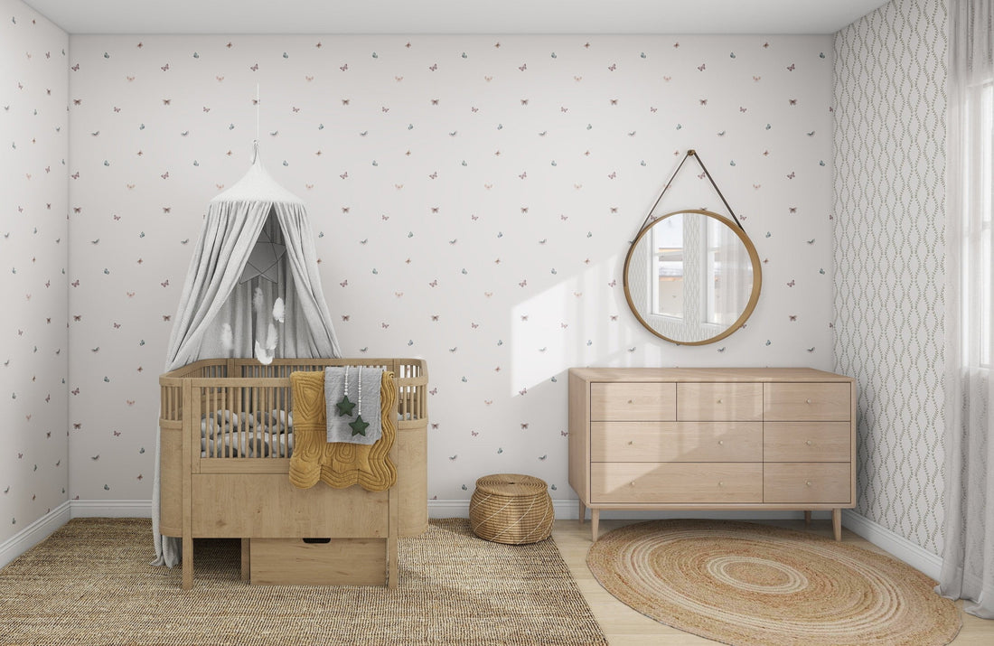 A cozy nursery features a wooden crib with a white canopy and munks and mes Bibi Butterflies Wallpaper. A natural wicker basket and circular rug decorate the floor, a round mirror hangs above the wooden dresser, all set against walls with subtle hand-drawn details.