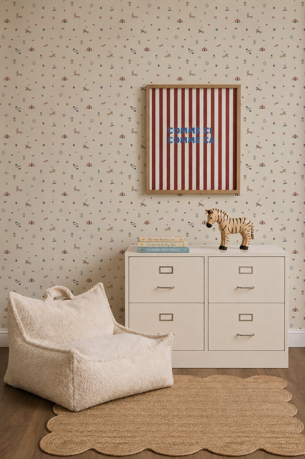 A cozy nursery corner features a white dresser, a plush cream chair, a scalloped rug, a toy tiger, and striped artwork. The walls are adorned with the Petite Circus Party Wallpaper, lending an elegant touch to the space. Two books rest on the dresser.