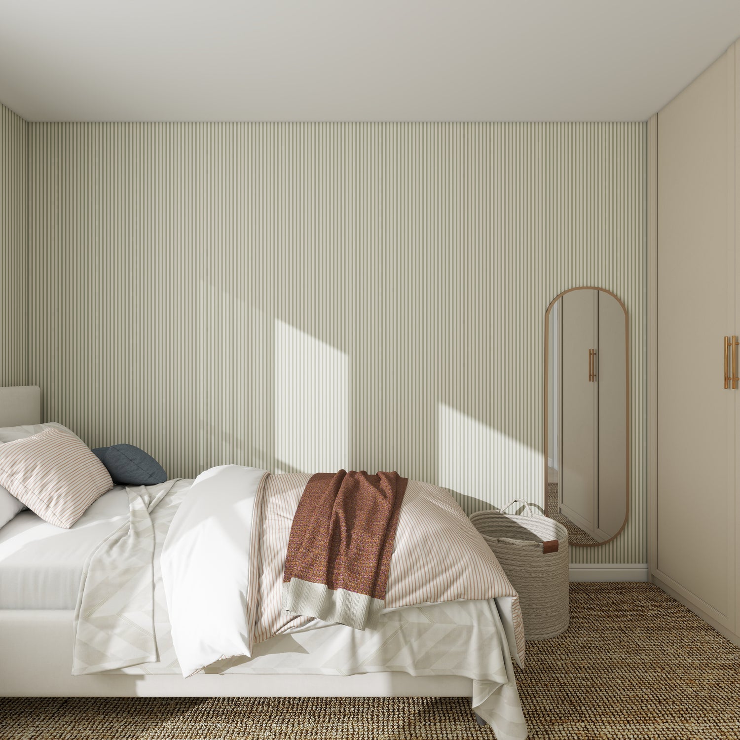 A minimalist bedroom features a neatly made bed with striped bedding and a brown throw, accented by a tall oval mirror and small woven basket against Pico Stripe Wallpaper Green, with sunlight streaming in.